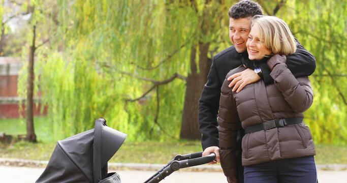 Happy man embraces woman near baby carriage in fall park