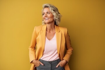 Portrait of happy mature businesswoman in yellow suit looking away over yellow background