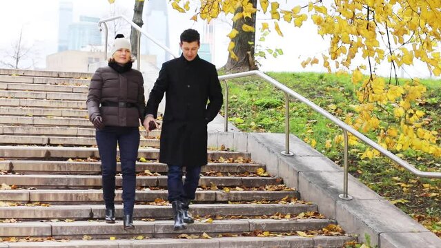 Happy man and pretty woman in hat down on stairs in fall park