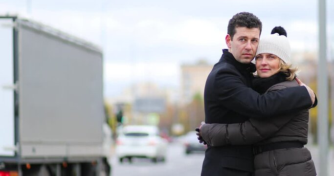Man and pretty woman stands and hug near city road at autumn day, shallow dof
