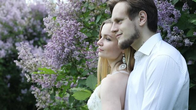 Woman and man turn in park with lilac at sunny day, slow motion