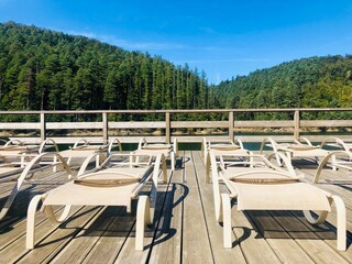 Fototapeta premium Empty sunbeds on a wooden pontoon near a lake surrounded by green forest