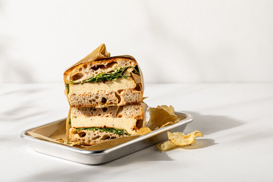 Breakfast sandwich wrapped in paper on white plaster background
