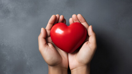 Fototapeta premium Hands holding a red heart on a grey background with copy space. Top view, st Valentine day concept. Minimal abstract composition for 14 February celebration