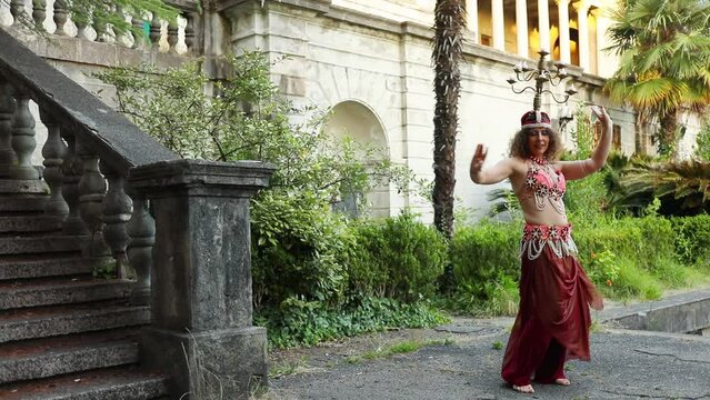 Woman in red costume dances belly dance with chandelier on head in tropical garden of Ordzhonikidze sanatorium, Sochi, Russia