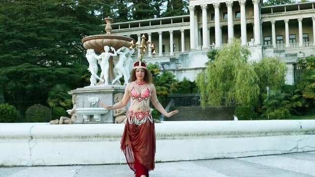 Woman dances belly dance with chandelier on head near fountain in Ordzhonikidze sanatorium, Sochi, Russia