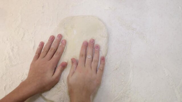Child hands knead soft dough for baking at home on table, top view