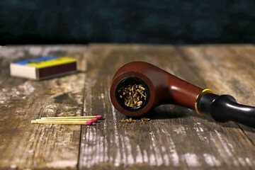 Smoking pipe filled with tobacco and matches on a rough wooden background.