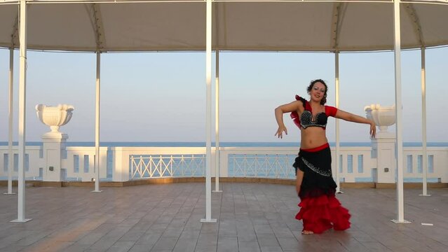 Woman dances belly dance in flamenco costume at stage near blue sea