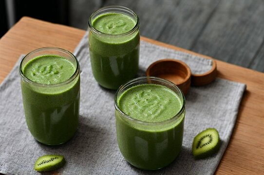 Healthy green smoothie in glass jars with straws on table