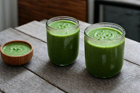Healthy green smoothie in glass jars with straws on table