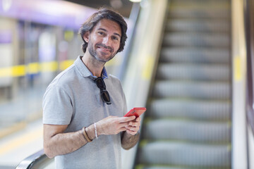 View of young man using a smartphone inside a subway - metro station with a blurred view landscape in the background. High quality video. Texting, talking on the phone. 