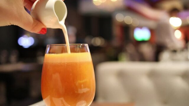 Female hand pours cream in orange cocktail in restaurant, slow motion