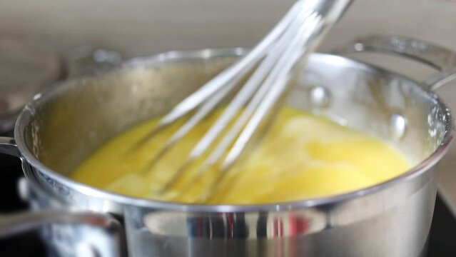 Hands mixes yellow cream for cake in pot, close up, slow motion