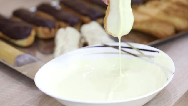 Female hands make eclairs with chocolate and white icing, close-up, slow motion