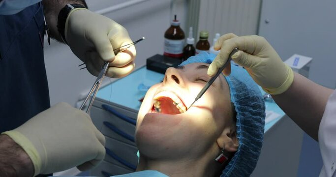 Face of patient, hands of dentist sutured wound after tooth extraction and assistant with dental instruments