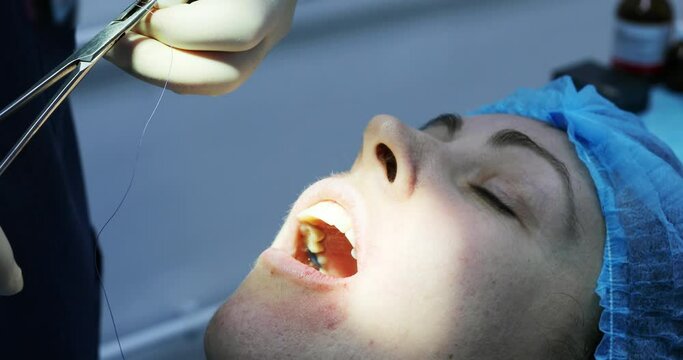 Face of patient, hands of dentist sutured wound after tooth extraction