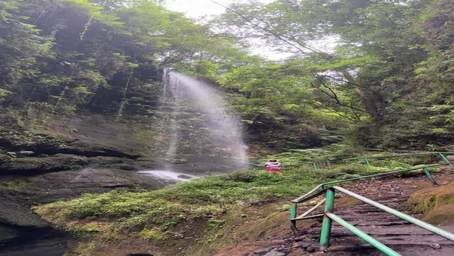 Young woman filming a amazing waterfall in the middle of the jungle with her mobile phone after a trekking. Cascada de los Tilos, La Palma, spain