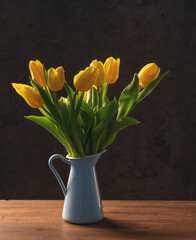 beautiful tulips in a blue vase on a dark wooden table on a dark background