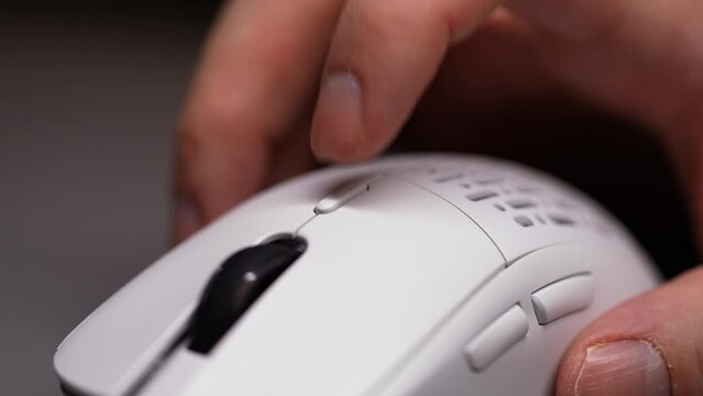 Closeup cropped shot of unrecognizable man clicking modern wireless computer mouse, changing DPI by buttons, sitting at desk in dark room with cozy light. Shooting in slow motion.