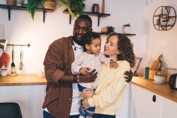 Multiethnic family with child in kitchen together and embracing each other