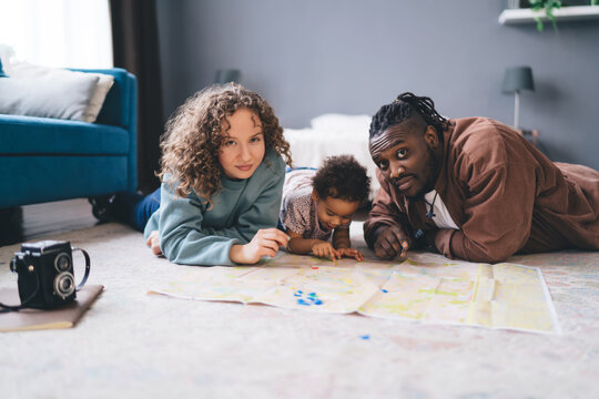 Diverse parents looking at camera while kid drawing on paper in living room