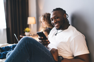 Cheerful bearded black man sitting with family while browsing smartphone