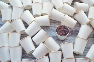 White paper cups scattered on the table and one with coffee beans among them. Coffee beans in a...