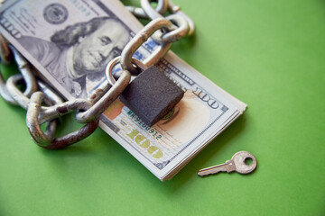 A chain and a closed lock lay on a stack of hundred dollar bills next to the key, locking up money,...