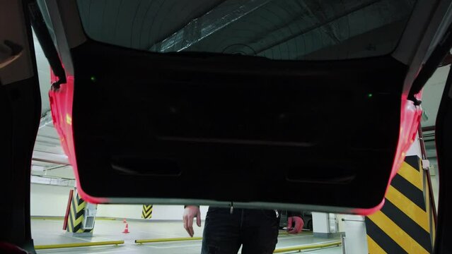 Man in black clothes closes car boot on underground parking
