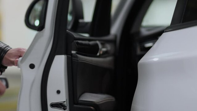 Man in black jacket opens and closes door of white modern car