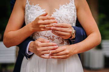 Valmiera, Latvia - July 7, 2023 - Close-up of a bride and groom's hands with wedding rings, over the bride's lace dress.