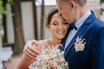 Valmiera, Latvia - July 7, 2023 - Bride and groom embrace, the bride smiling and holding a bouquet,...