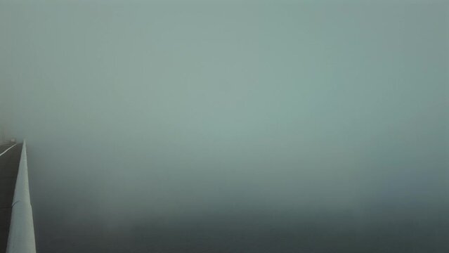 A large suspension bridge over the sea bay covered with fog or haar. Video with the panning camera motion. Forth Road Bridge, Scotland, United Kingdom