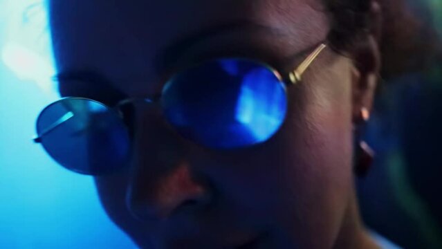 Woman in round glasses moves dances in dark night club with colorful illumination