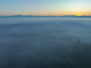 Obraz premium aerial view a sea of white mist envelops the mountain peak, slowly flowing down from the mountain peak...The mist poured down from the mountains in the morning...the sea of mist background.