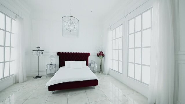 White bedroom interior with red head of bed and flowers among large windows in photo studio