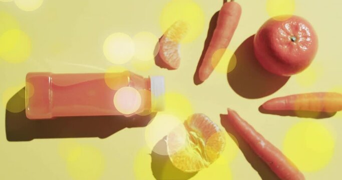Composition of spots of light over bottle of fruit juice, carrots and oranges on yellow background