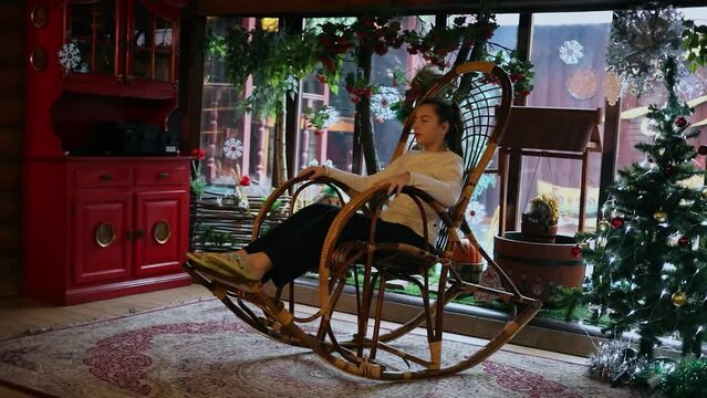 Young girl sways on rocking chair near christmas tree. Slow motion