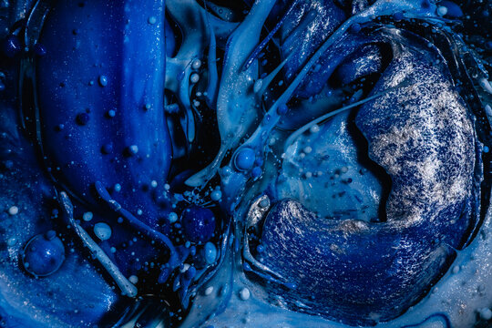 Intense dark and light blue ink swirls with speckles of white, creating an abstract oceanic texture with bubbles scattered throughout