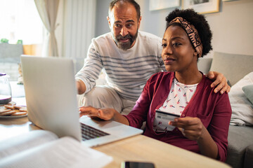 Diverse middle aged couple using laptop for online shopping at home