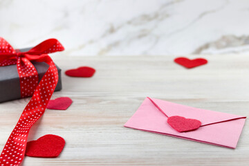 Valentine's Day concept: gift box with red ribbon, red hearts and pink paper envelope on a light background. flat lay