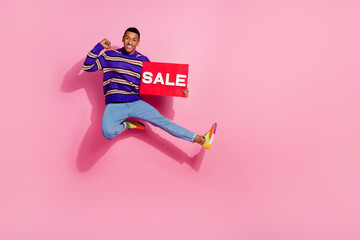 Full length photo of cheerful lucky guy dressed pullover jumping high rising fist holding sale card...