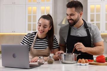 Fototapeta na wymiar Happy lovely couple using laptop while cooking in kitchen