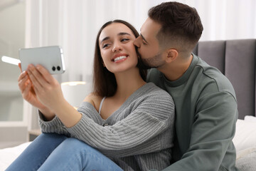 Happy young couple taking selfie in bedroom