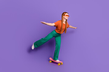 Fototapeta na wymiar Photo of shiny sweet cheerful girl dressed stylish clothes riding penny board looking empty space isolated on purple color background