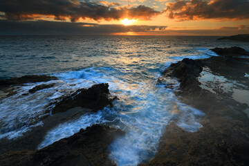 Dramatic sunset over rocky coastline with crashing waves