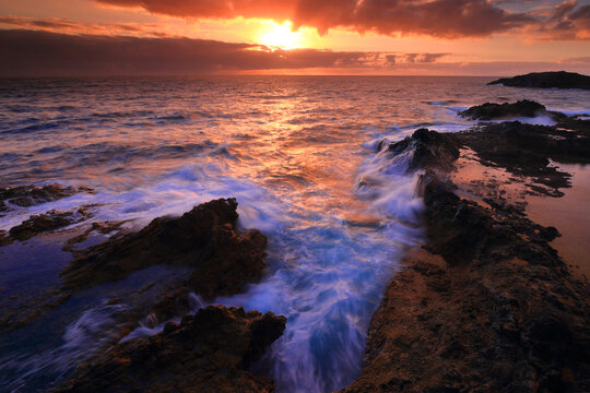 Sunset over rugged coastline with crashing waves