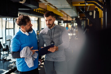 Middle aged man and his personal trainer going through exercise plans in gym.