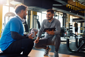 Fitness instructor using touchpad while talking to mature man during exercise class in gym.